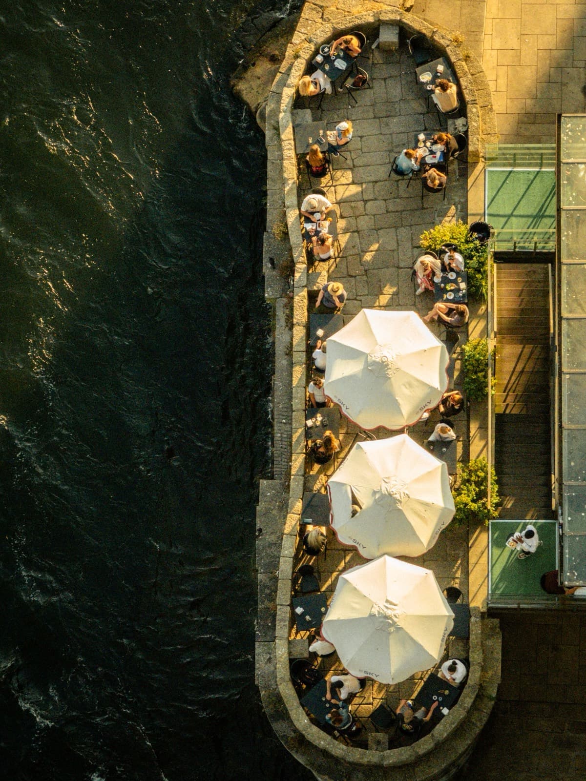 Waterfront restaurant terrace at golden hour, tables by the water